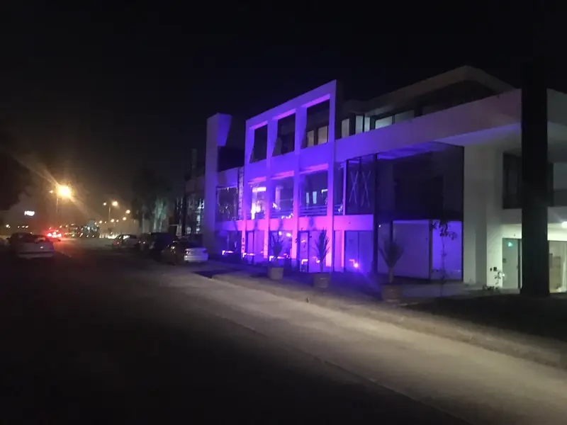 Fachada blanca del bulevar de noche, iluminada con luces moradas y rosadas