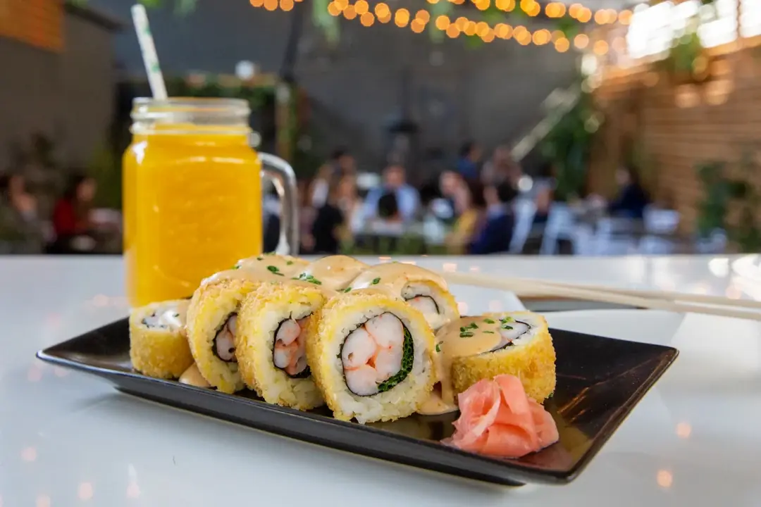 Rolls de sushi apanados con camarón y un jugo natural, en una mesa bajo guirnaldas de luces